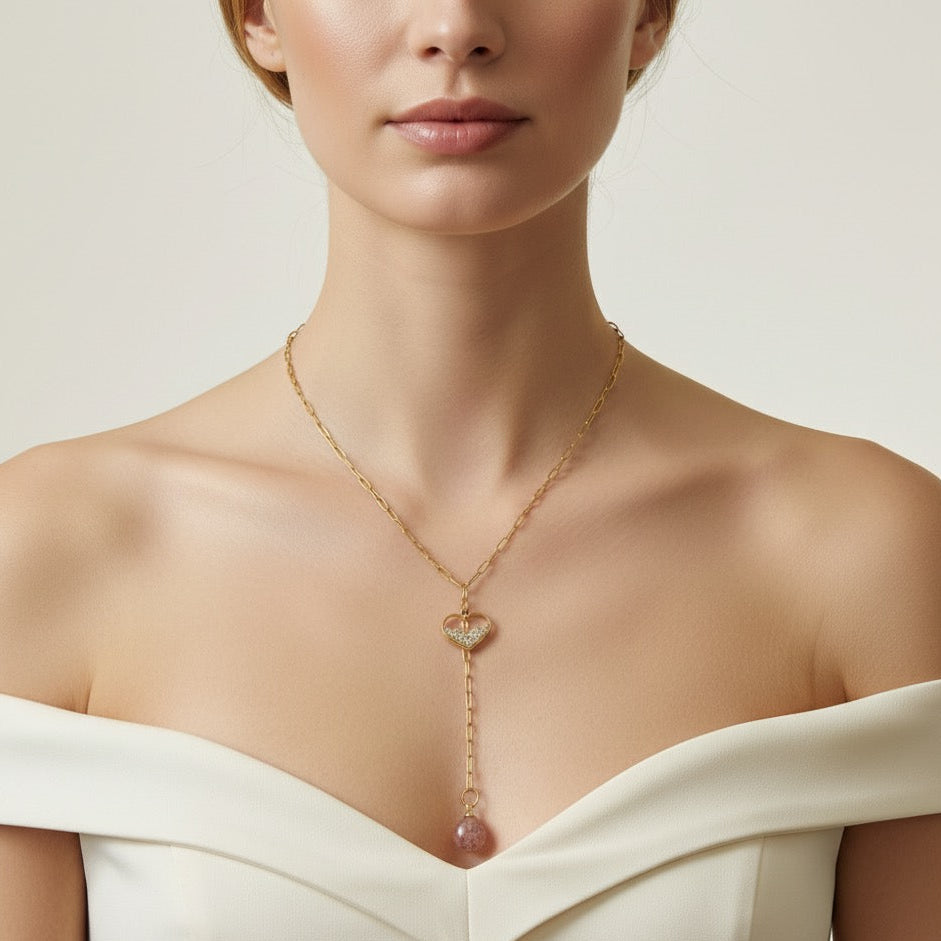 Woman wearing a gold necklace with a heart pendant and pink gemstone on a neutral background